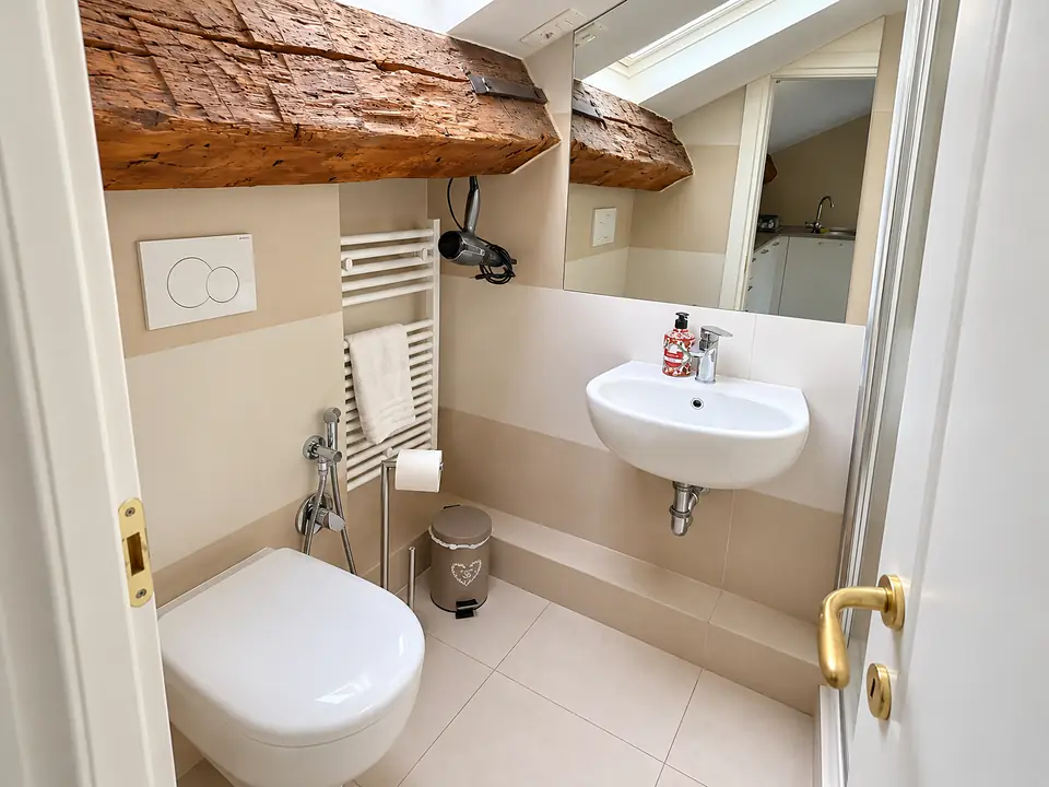 Bagno con lavabo, scaldasalviette e asciugacapelli sotto una trave antica