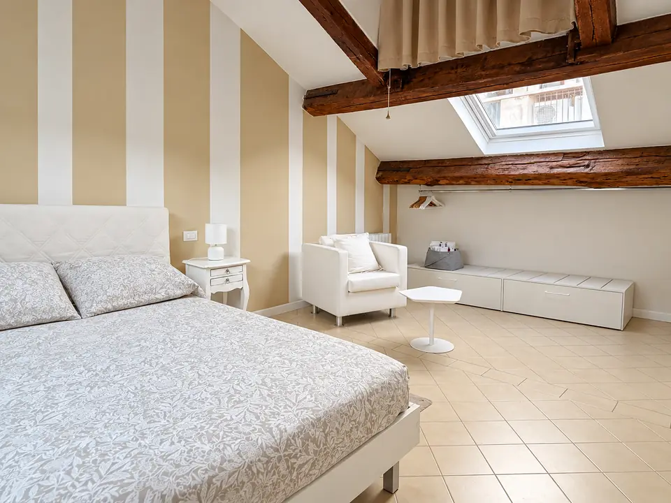 Camera con letto matrimoniale, poltrona bianca e pareti a righe sotto le travi a vista